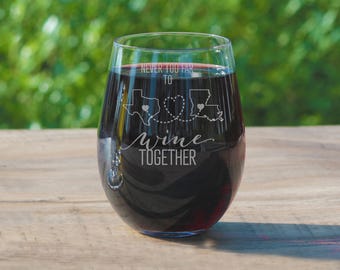 May include: A clear wine glass with a stem and a wide bowl. The glass is etched with the states of Texas and Louisiana, connected by a dotted line with a heart in the middle. The text "Never too far to wine together" is etched below the states.