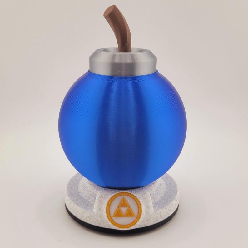 Op de afbeelding: Een blauw, bolvormig decoratief object met een bruine steel en een zilveren bovenkant. Het object staat op een witte basis met een gouden embleem. De basis heeft een zwarte onderkant.