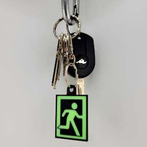May include: A black and green glow-in-the-dark keychain with a running person icon inside a square. The keychain is attached to a set of keys with a black car key fob.