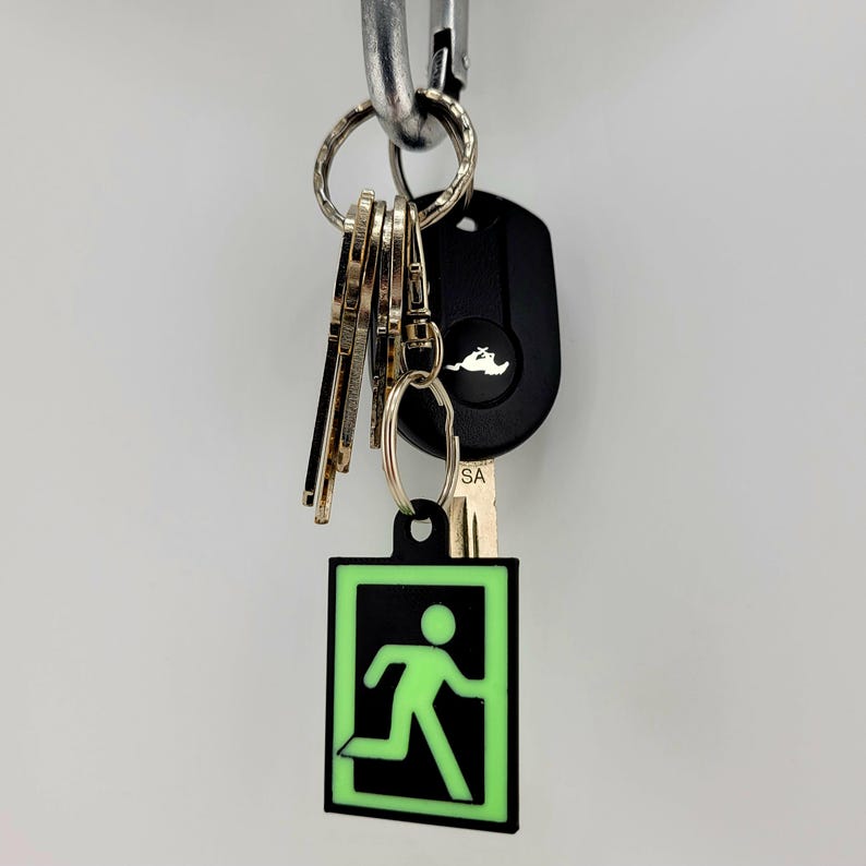 May include: A black and green glow-in-the-dark keychain with a running person icon inside a square. The keychain is attached to a set of keys with a black car key fob.