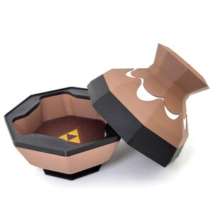 May include: A brown and black ceramic container with a lid. The lid has a white design and the container has a gold triangle symbol on the inside.