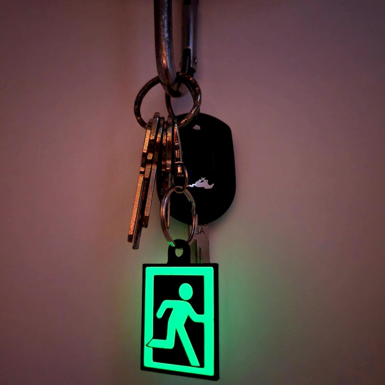 May include: A green exit sign keychain with a running person icon. The keychain is attached to a silver carabiner and a set of keys.