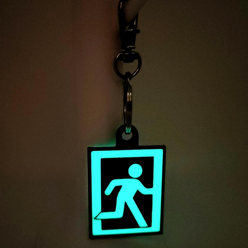 May include: A black keychain with a glow-in-the-dark green exit sign featuring a running person icon.