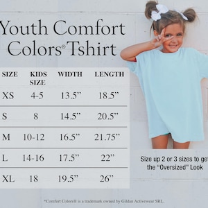 Puede incluir: Una camiseta Comfort Colors juvenil azul claro con una tabla de tallas. La tabla enumera las tallas XS a XL, con medidas de ancho de 34,3 cm a 49,5 cm y largos de 47 cm a 66 cm. Una ni&ntilde;a peque&ntilde;a que lleva la camiseta est&aacute; en la imagen.