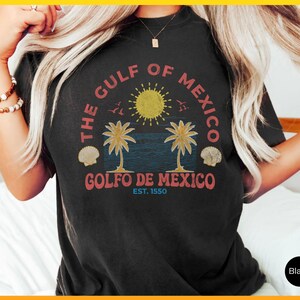 K&ouml;nnte beinhalten: Schwarzes T-Shirt mit einem Vintage-Grafikdruck einer Sonne, Palmen und Muscheln. Der Text lautet "The Gulf of Mexico, Golfo de Mexico, Est. 1550".