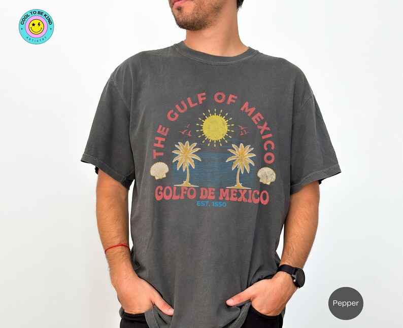 K&ouml;nnte beinhalten: Ein dunkelgraues T-Shirt mit einem grafischen Aufdruck von Palmen und einer Sonne. Der Text "The Gulf of Mexico" und "Golfo de Mexico Est. 1550" ist auf dem T-Shirt aufgedruckt.
