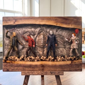 Peut inclure: Un panneau de présentation rectangulaire en bois à bord brut avec une incrustation centrale en résine contenant quatre figurines de personnages de films d'horreur debout sur un lit de crânes miniatures, incluant un tueur masqué et un clown.
