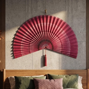May include: A large, semi-circular wall-mounted folding fan featuring a gradient of deep red and magenta tones. The fan is constructed with pleated material and includes a matching red decorative tassel hanging from the center point at the bottom.