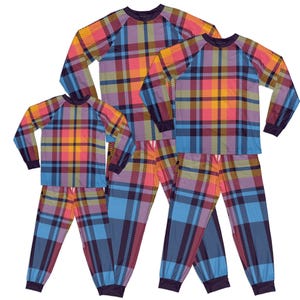 Op de afbeelding: Een set van drie bijpassende pyjama's met een kleurrijk ruitpatroon in tinten blauw, roze, geel en paars. De pyjama's hebben lange mouwen en een ronde hals.