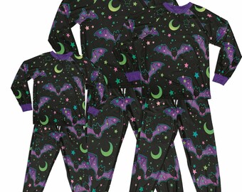 May include: A set of black pajamas with a purple trim. The pajamas feature a repeating pattern of bats, stars, and crescent moons. The pajamas are available in different sizes.