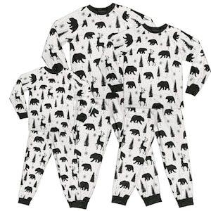 May include: A set of three white pajamas with a black and white pattern of bears, deer, and trees. The pajamas have long sleeves and long pants.