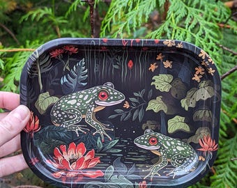 May include: Black rectangular tray with a detailed illustration of two green frogs with red eyes, surrounded by red flowers and lily pads. The tray has a dark background with a forest theme.