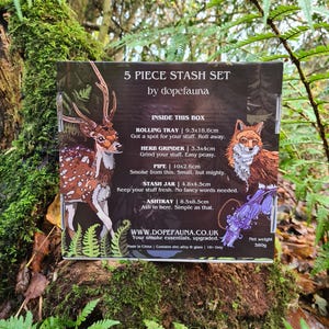 May include: A 5-piece stash set by dopefauna, featuring a deer and fox illustration. Includes a rolling tray (9.3x18.6cm), herb grinder, pipe, stash jar, and ashtray. The box is set against a natural, mossy background.