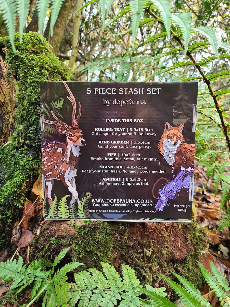 May include: A 5-piece stash set by dopefauna, featuring a deer and fox illustration. Includes a rolling tray (9.3x18.6cm), herb grinder, pipe, stash jar, and ashtray. The box is set against a natural, mossy background.