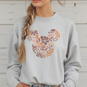 Pu&ograve; includere: Una felpa grigia con un design floreale di Topolino in tonalit&agrave; arancio, rosa e marrone.