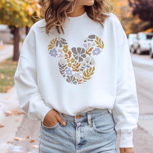 Pu&ograve; includere: Felpa bianca con un design floreale di Topolino in tonalit&agrave; gialle, marroni e viola.