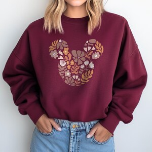 Pu&ograve; includere: Felpa color borgogna con un design floreale di Topolino. I fiori sono in tonalit&agrave; di marrone, giallo e rosa.