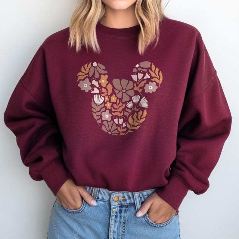 Pu&ograve; includere: Felpa color borgogna con un design floreale di Topolino. I fiori sono in tonalit&agrave; di marrone, giallo e rosa.