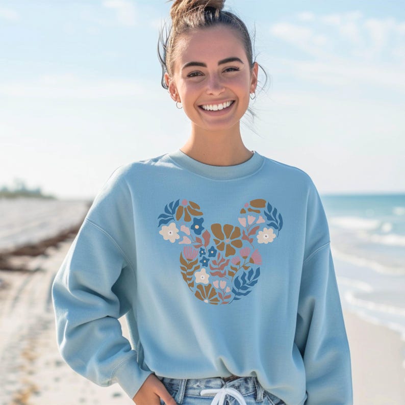 Pu&ograve; includere: Una felpa blu chiaro con un design floreale di Topolino. Il design &egrave; in tonalit&agrave; di blu, marrone, rosa e bianco.