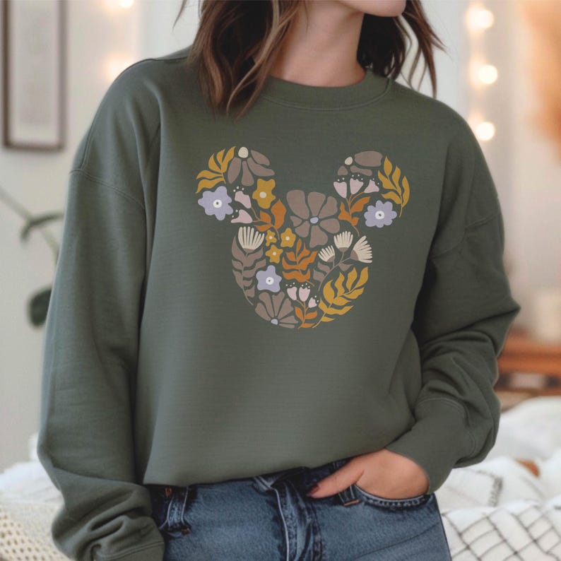 Pu&ograve; includere: Una felpa verde con un design floreale di Topolino. I fiori sono in tonalit&agrave; di giallo, arancione, rosa e viola.