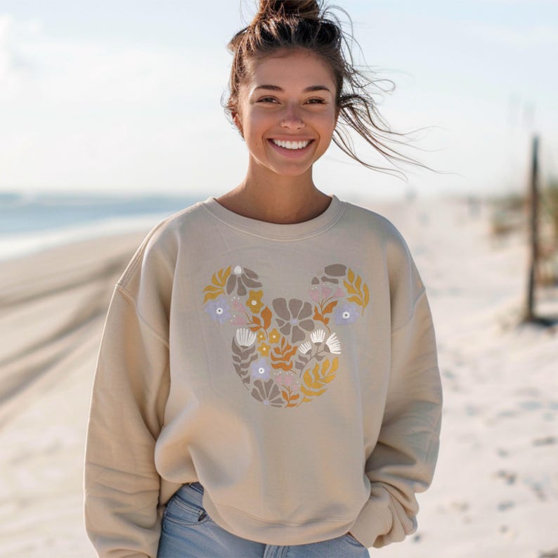 Pu&ograve; includere: Una felpa beige con un design floreale di Topolino. I fiori sono in tonalit&agrave; di giallo, arancione, rosa e viola.