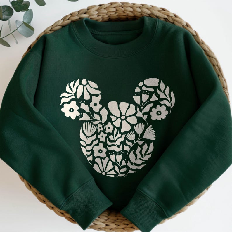 Pu&ograve; includere: Una felpa verde scuro con un design floreale di Topolino bianco.