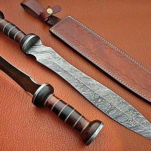 May include: A Damascus steel sword with a brown wooden handle and a leather sheath. The sheath has a decorative pattern and the text "R 321" is visible on the top right corner.
