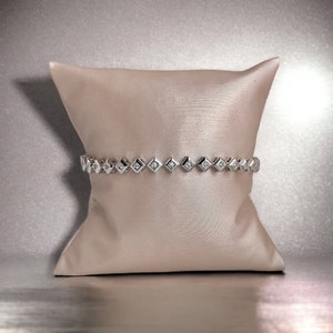 Pode incluir: Uma pulseira de prata com uma fileira de pequenos diamantes quadrados engastados em um design delicado.