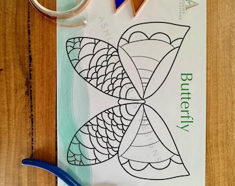May include: A craft kit with a butterfly design, including a roll of copper foil tape, colorful glass pieces, and pliers. The butterfly template is printed on a white paper with the word "Butterfly" in green.