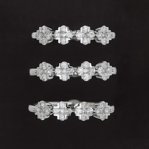 Puede incluir: Tres anillos de plata, cada uno con una serie de diseños de tréboles de cuatro hojas incrustados con pequeños diamantes brillantes. Los anillos se muestran sobre un fondo negro, resaltando su brillo.