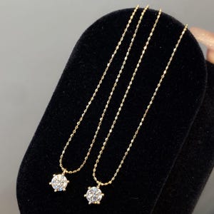 May include: Two gold necklaces with a round, clear gemstone pendant. The necklaces are displayed on a black velvet surface. The chains have a delicate, beaded design.
