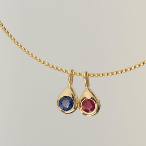 Könnte beinhalten: Eine goldene Kettenkette mit zwei Anhänger in Tropfenform. Ein Anhänger hat einen blauen Edelstein und der andere einen roten Edelstein.