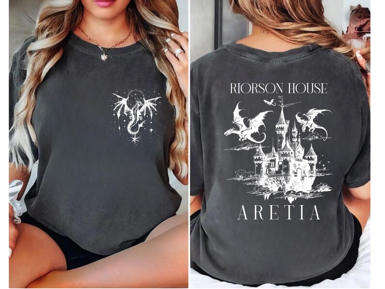 May include: Dark gray t-shirt with a white dragon and star design on the front. The back features a castle illustration with dragons, the text "RIORSON HOUSE" above, and "ARETIA" below. A fantasy-themed graphic tee.