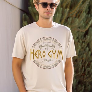 A man wearing a white t-shirt with a graphic design and text printed on it, standing in front of a background of greenery.