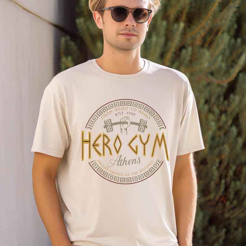 A man wearing a white t-shirt with a graphic design and text printed on it, standing in front of a background of greenery.