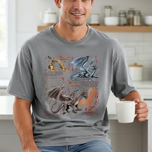 Peut inclure: T-shirt gris avec des illustrations d&eacute;taill&eacute;es de dragons dor&eacute;s, argent&eacute;s et bleus. Le motif comprend du texte et des croix, cr&eacute;ant un th&egrave;me fantastique. Le t-shirt est un v&ecirc;tement d&eacute;contract&eacute; et confortable.