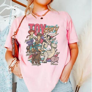 A woman wearing a pink t-shirt with a graphic design featuring characters from the Toy Story movie.