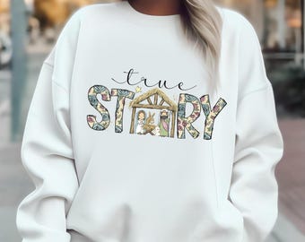 Puede incluir: Sudadera blanca con el texto "true STORY" en un estampado floral. La palabra "STORY" presenta una ilustración del nacimiento. La sudadera es de cuello redondo.