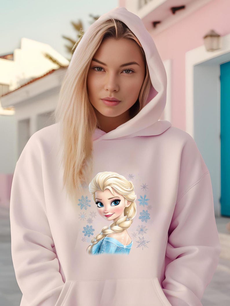 May include: A pink hoodie with a graphic of a cartoon princess with blonde hair and a blue dress. The princess is surrounded by snowflakes.