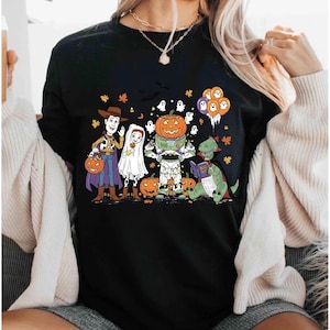 A woman wearing a black t-shirt with a Halloween-themed graphic design featuring characters from Toy Story, including Woody, a pumpkin, and other spooky elements.