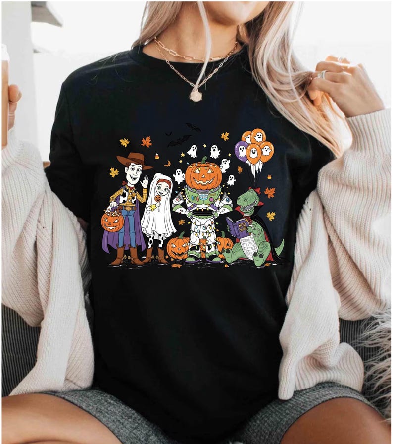 A woman wearing a black t-shirt with a Halloween-themed graphic design featuring characters from Toy Story, including Woody, a pumpkin, and other spooky elements.