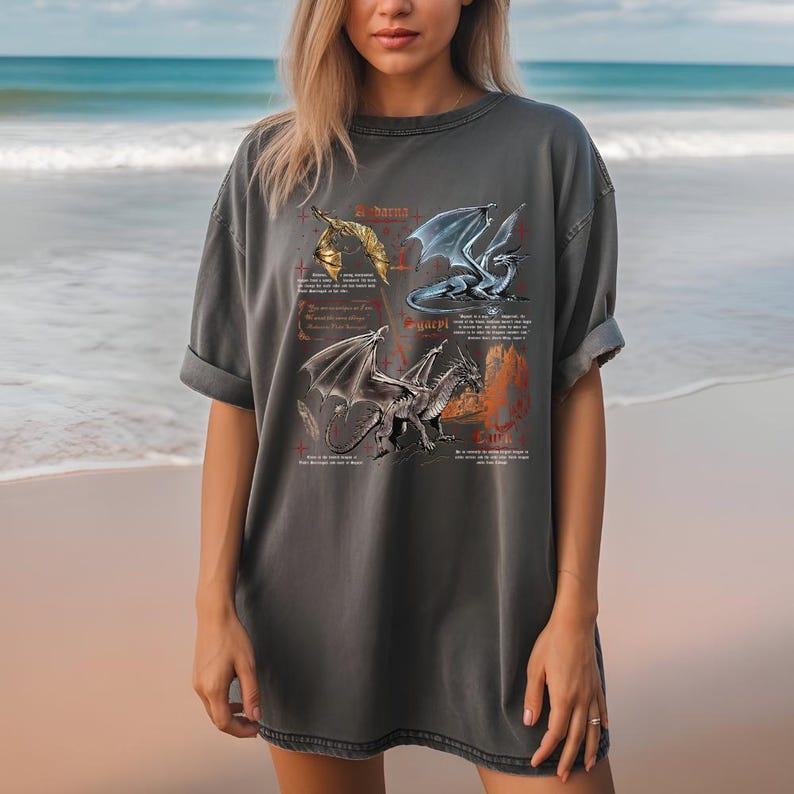 Peut inclure: T-shirt gris fonc&eacute; avec quatre illustrations de dragons et du texte. Les dragons sont repr&eacute;sent&eacute;s en or, bleu et gris, dans diff&eacute;rentes poses. Le t-shirt a des manches courtes et une coupe d&eacute;contract&eacute;e.
