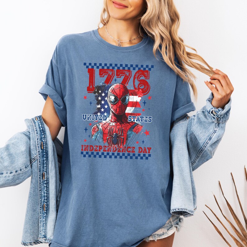 May include: Blue t-shirt featuring a graphic of Spider-Man with the American flag and the text "1776 United States Independence Day". The design incorporates red, white, and blue colors.