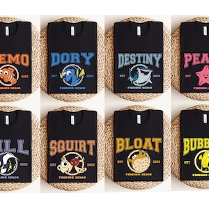May include: Black t-shirts featuring characters from the movie "Finding Nemo." Each shirt displays a character's name in a collegiate font, with the character's image and the text "EST 2003 FINDING NEMO."