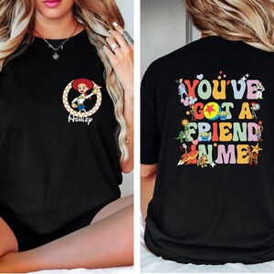 May include: Black t-shirt featuring a cartoon image of Jessie from Toy Story with the name "Ashley" below. The back of the shirt has the phrase "You've Got A Friend In Me" with various Toy Story characters.