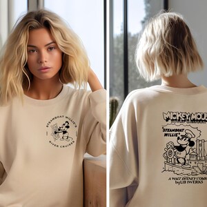 May include: A beige sweatshirt with a black and white graphic of Mickey Mouse on a steamboat. The text "Mickey Mouse" and "Steamboat Willie" is printed on the sweatshirt. The text "A Walt Disney Comic by UB Iwerks" is also printed on the sweatshirt.