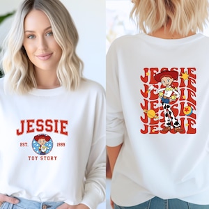 May include: White long-sleeve shirt featuring the name "JESSIE" in red collegiate lettering. The front design includes a cartoon image of Jessie from Toy Story, with "EST. 1999" and "TOY STORY" below. The back displays a larger Jessie graphic.
