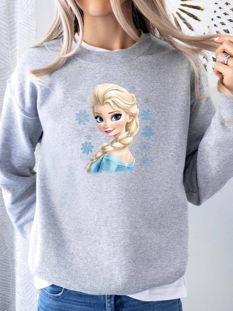 May include: Gray sweatshirt with a printed image of Elsa from Frozen. Elsa is wearing a blue dress and has long blonde hair. There are snowflakes around her.
