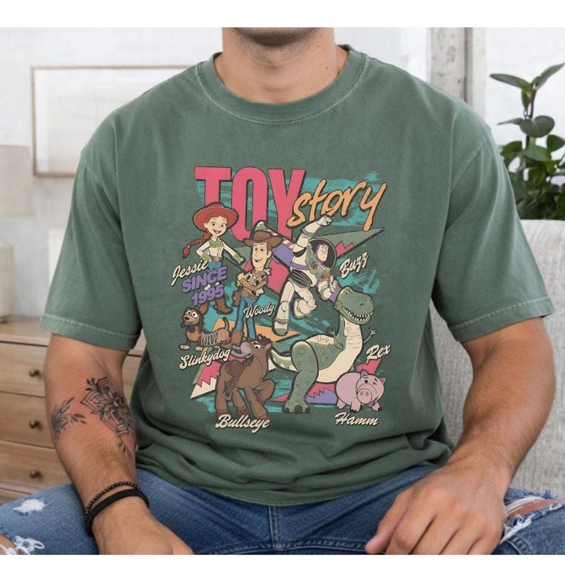 A person wearing a green t-shirt with a colorful graphic design featuring characters from the Toy Story movie.