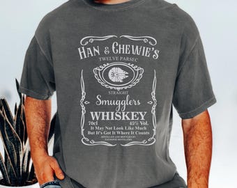 May include: A gray t-shirt with a vintage-style whiskey label design featuring the text "Han & Chewie's Twelve Parsec Straight Smugglers Whiskey 70cl 45% Vol. It May Not Look Like Much But It's Got It Where It Counts Distilled and Bottled by Tatooine Distillery".